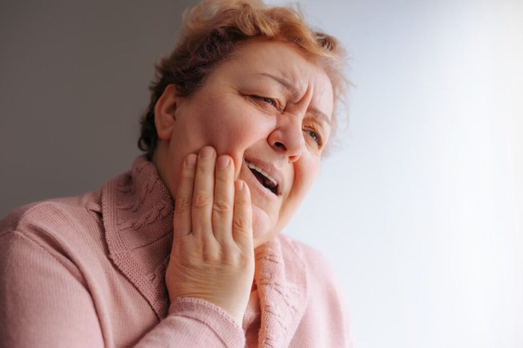 Woman experiencing tooth pain, holding her cheek in discomfort and wincing.