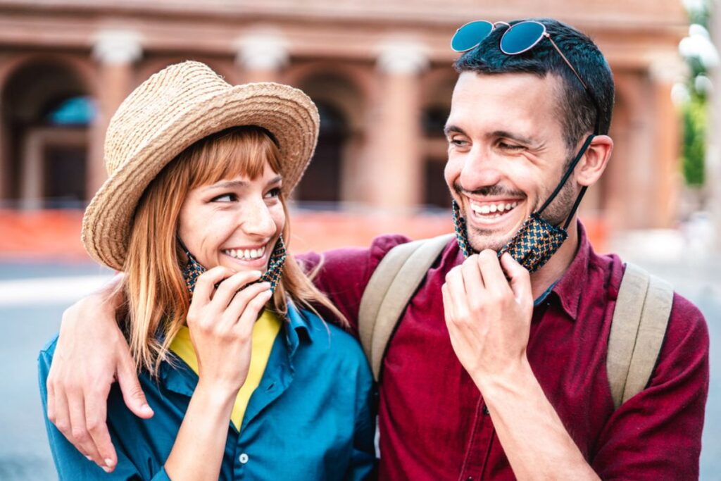 Smiling couple wearing colorful casual outfits and fun accessories celebrate teeth whitening results.