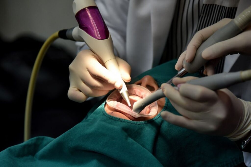 Emergency dentist performing oral surgery with specialized laser equipment on patient.