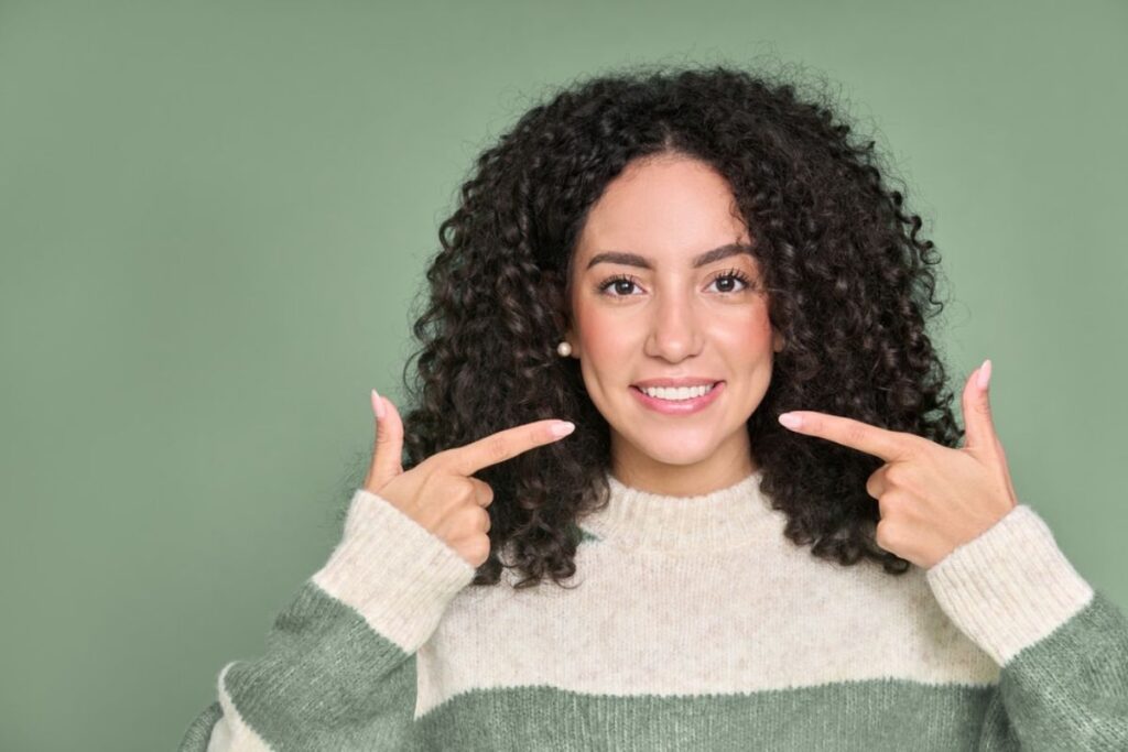 Woman smiling with bright white teeth wearing green and cream striped sweater.