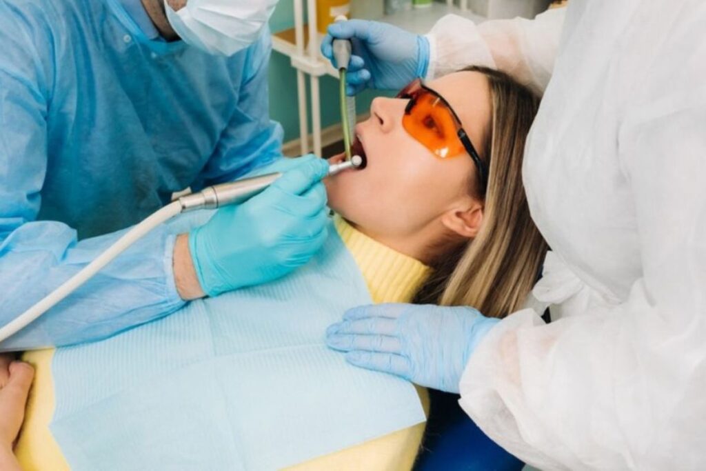Dentist performing laser teeth whitening treatment on young patient wearing protective eyewear.