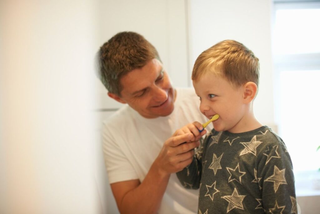Father helping young child brush teeth with proper technique.