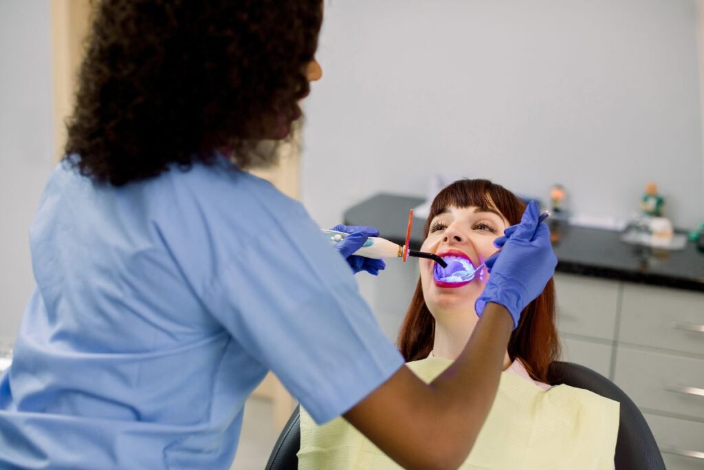 Dentist in blue gloves examining patient's teeth during professional whitening treatment.