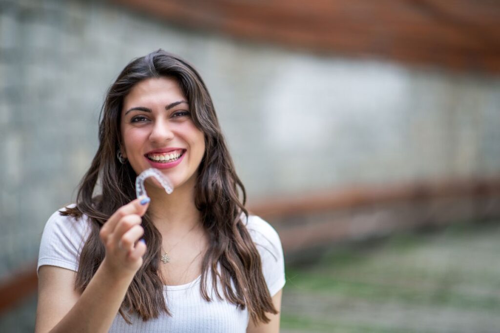 A woman holding an Invisalign aligner with a bright smile.
