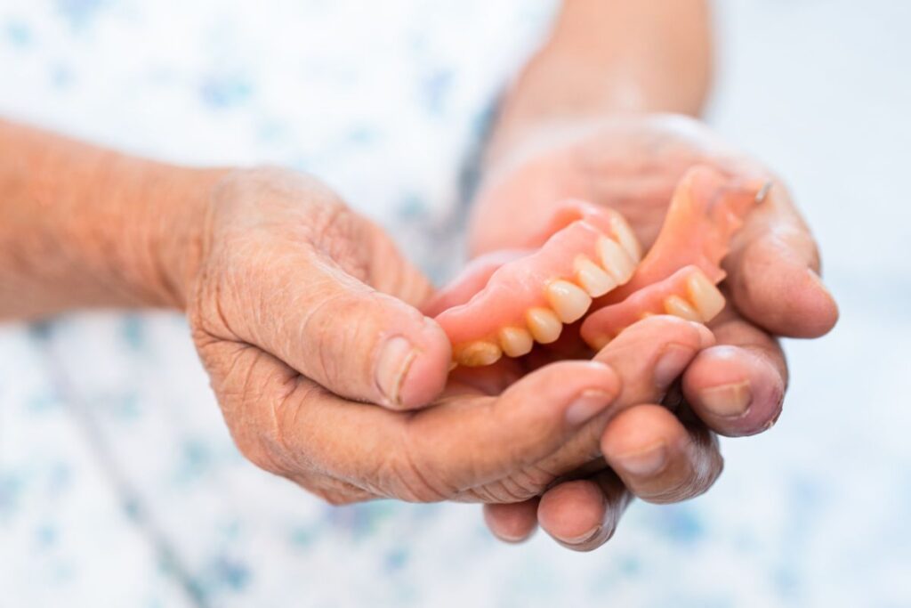 Elderly person holding a set of removable dentures.