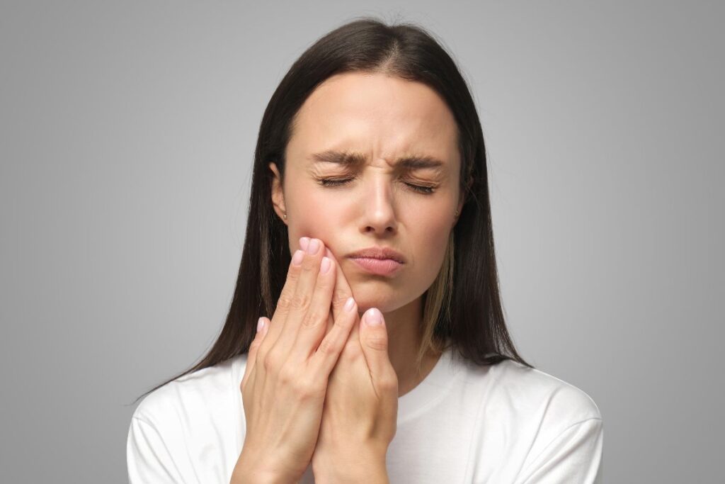 A woman touching her jaw due to stress-related tooth pain.