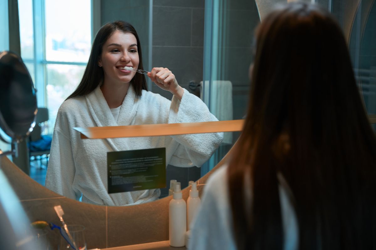 Woman brushing her teeth in a hotel bathroom while getting ready.