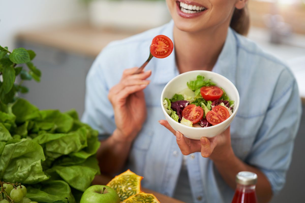 Woman enjoying a bowl of fresh vegetables promoting oral health and strong teeth.