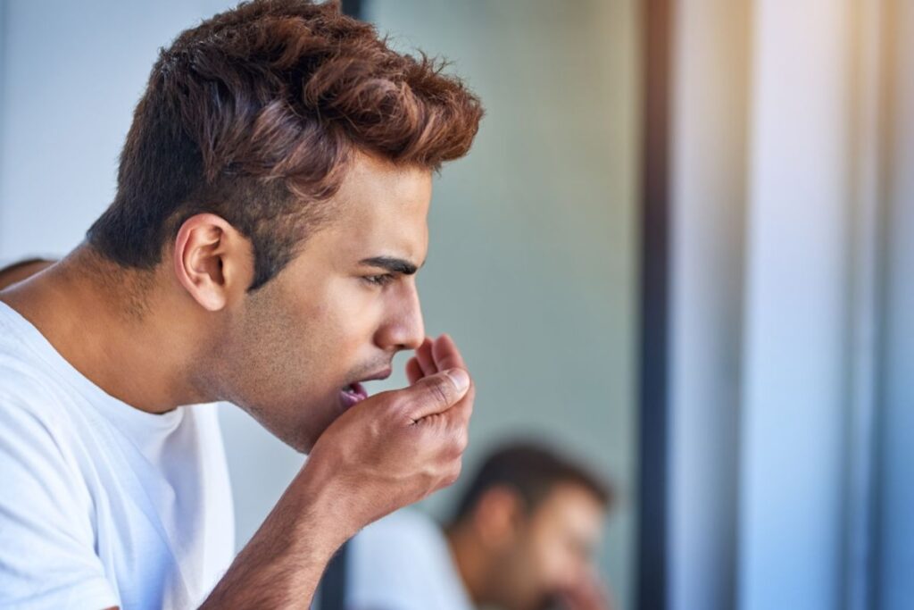 Man checking his breath in the mirror, highlighting common causes of bad breath and the importance of oral hygiene for fresher breath.