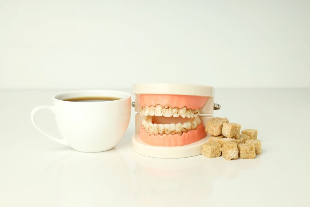 Dental model with stained teeth beside coffee and sugar cubes, illustrating sugar’s impact on oral health.