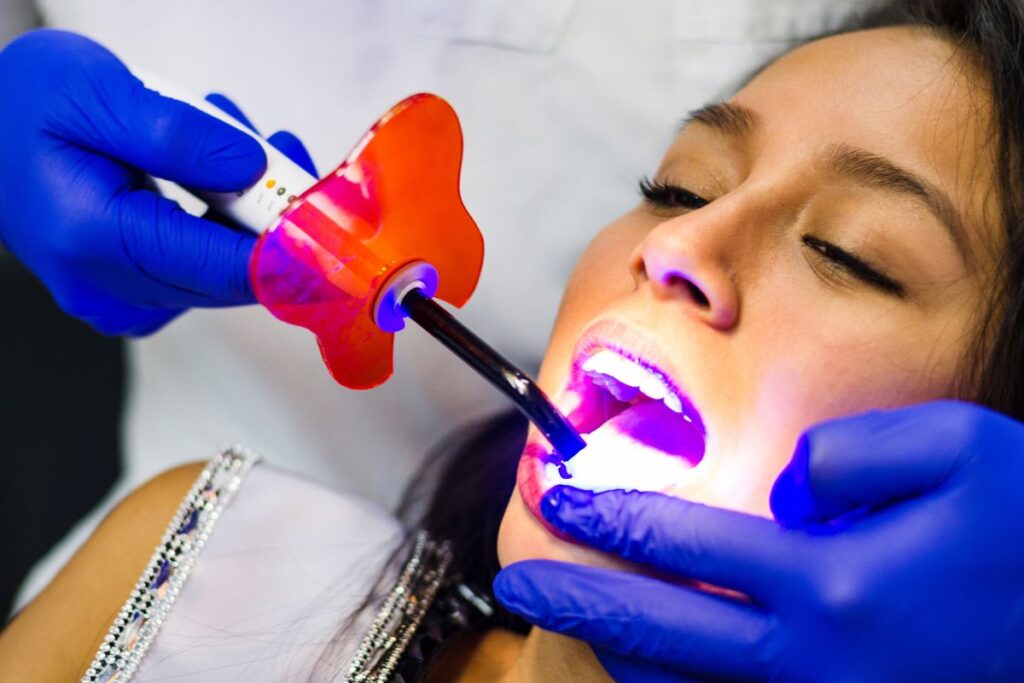 Dentist applying professional whitening treatment to patient's teeth with UV light technology.