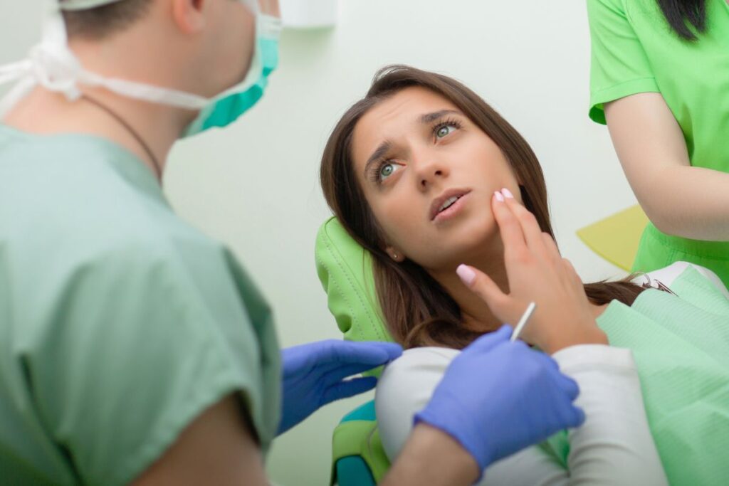 Woman with toothache touching her cheek during dental examination with dentist and hygienist.